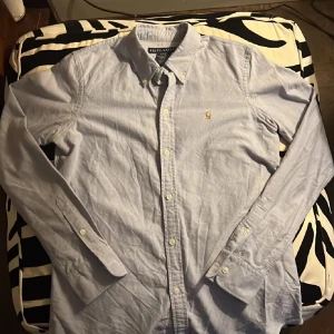 Ljusblå skjorta från Ralph Lauren - Säljer en stilren ljusblå skjorta från Ralph Lauren i slim fit-modell. Skjortan är i 100% bomull, har klassisk krage, knäppning framtill och det ikoniska broderade logotypen på bröstet. Perfekt för dig som gillar en clean och tidlös look.