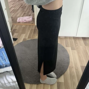 Svart långkjol med slits - Säljer en svart långkjol med tight passform och slits på sidan. Kjolen är enkel och stilren, perfekt om du gillar minimalistisk look. Materialet känns mjukt och följsamt mot kroppen. Passar dig som vill ha en klassisk svart kjol med lite edge. Säljer då den är för kort