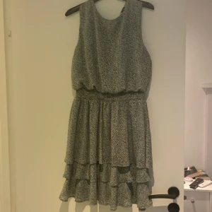 Grön  leopardmönstrad volangklänning - Snygg ärmlös kortklänning i grön med leopardmönster och flera volanger i kjolen. Klänningen har resår i midjan och en liten knapp i nacken. Perfekt för dig som gillar djurmönster och vill ha en luftig och trendig look.