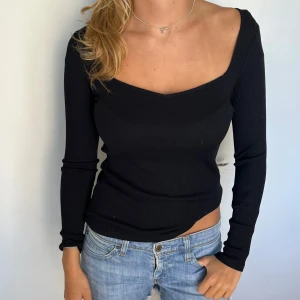 Svart ribbad långärmad topp - Svart långärmad topp med djup v-ringning och ribbad struktur. Sitter tight och har en stilren, enkel design som passar till jeans eller kjol. Perfekt för dig som gillar en klassisk men ändå trendig look.
