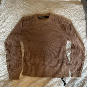 Beige stickad tröja Black Label S - Snygg beige stickad tröja från lager 157 i storlek S. Tröjan har rund halsringning, ribbade muddar och nederkant samt långärmad passform. Perfekt för lager-på-lager och chill höst- eller vinterstil.