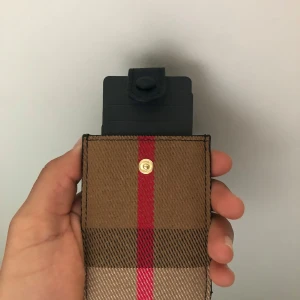 Rutig plånbok med röd detalj - Snygg plånbok i klassiskt rutigt mönster med bruna och beige toner samt en röd rand i mitten. Plånboken har svart knappstängning upptill och är tillverkad i ett tåligt material. Perfekt för kort och småsaker, stilren och enkel att ta med sig.