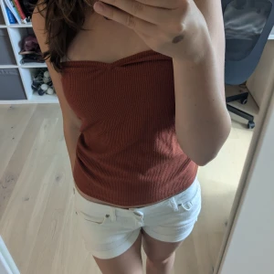 Rostbrun ribbad tubtopp - Säljer en snygg rostbrun ribbad tubtopp i bandeau-modell. Toppen är ärmlös och har en tight passform som sitter på plats. Materialet är mjukt och stretchigt, perfekt för varma dagar. En liten silverring-detalj som tyder på att det är märket stockh lm.