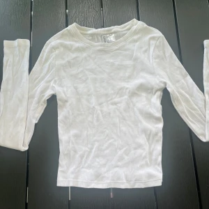 Vit ribbad långärmad tröja DIVIDED - En basic vit långärmad tröja från DIVIDED i ribbat material. Tröjan har rund halsringning och sitter tajt mot kroppen, perfekt att styla med jeans eller kjol. Enkel och stilren design som funkar till allt.