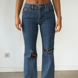 Blå bootcut jeans med slitna knän - Snygga blå jeans med bootcut passform och slitna detaljer vid knäna. Klassisk femficksmodell med hög midja och raka sömmar framtill. Jeansen har en cool vintage vibe och är perfekta för dig som gillar en avslappnad men trendig stil.