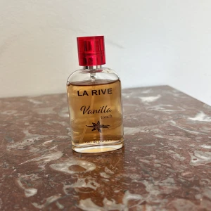 La Rive Vanilla Touch parfym - La Rive Vanilla Touch är en eau de parfum med söt vaniljdoft. Flaskan är genomskinlig med ljusgul vätska och har en stilren, rektangulär form. Korken är metallicröd och ger en snygg kontrast till flaskan. Perfekt för dig som älskar varma, mjuka dofter. 