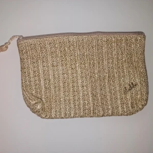Beige kuvertväska i stickad look - Snygg kuvertväska från med stickad känsla och grov struktur. Perfekt för att bära småsaker eller smink. Enkel och stilren design som sticker ut.