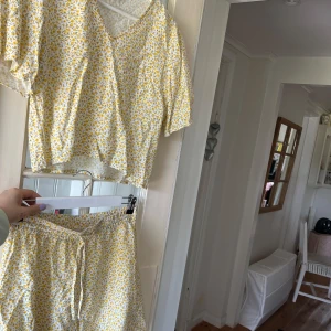 Blommiga shorts och T-shirt från Bubbleroom - Supersöta shorts och T-shirt  från Bubbleroom i vitt med små gula blommor och gröna detaljer. De har elastisk midja och snörning för extra komfort. Perfekta för varma dagar och ger en fräsch sommarkänsla. Lätta och luftiga i bomullsmaterial.