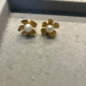 Guldiga blomörhängen med pärla - Snygga örhängen i form av blommor med guldiga kronblad och en vit pärla i mitten. Perfekta för att ge din look en söt och elegant touch. Stiftmodell som sitter bekvämt på örat. De är handgjorda!💕