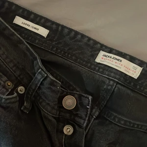 Svarta loose fit jeans Jack & Jones - Säljer ett par svarta jeans från Jack & Jones , modellen heter Chris. Jeansen har klassisk femficksdesign, knappar i gylfen och är tillverkade i bomull. Perfekta för dig som gillar en avslappnad och bekväm stil. Storlek 30,32