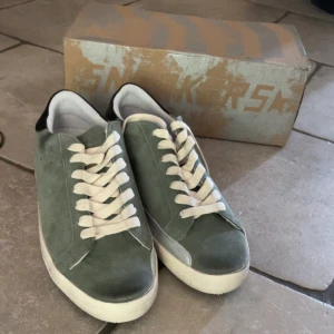 Gröna mockasneakers från Golden Goose - Snygga sneakers från Golden Goose i grön mocka med vita snören och vit sula. Skorna har svart detalj på hälen och klassisk låg profil. Perfekta för dig som gillar stilrena och trendiga sneakers med en unik touch.