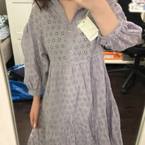 Ljuslila broderad klänning Pull&Bear - Superfin ljuslila kortklänning från Pull&Bear med broderade blommor och knappar framtill. Klänningen har trekvartsärmar med resår och volang nertill. Perfekt för vår och sommar, i luftig bomull som känns skön mot huden.