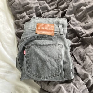 Grå Levi's Premium jeans straight fit - Säljer ett par grå Levi's Premium jeans med klassisk femficksdesign och rak passform. Jeansen har en snygg vintagegrå tvätt, brunt läderpatch bak och är tillverkade i slitstarkt bomullsjeans. Perfekta för dig som gillar en clean och tidlös look.