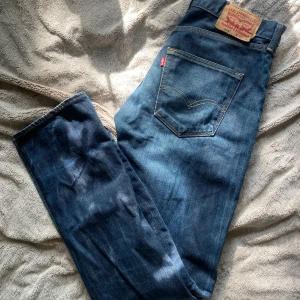 Levi's 501 blå jeans straight fit - Klassiska Levi's 501 jeans i mörkblå denim med raka ben och snygga slitningar. Jeansen har fem fickor, gylf med knappar och ikonisk läderpatch bak. Perfekta för en man mellan 190 och 210 cm. Passar min kille som är 2 meter perfekt!
