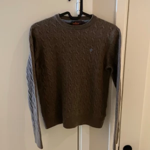 Brun kabelstickad merinoulltröja morris - Snygg brun kabelstickad tröja från Morris i storlek S. Tröjan har rund halsringning, lång ärm och diskret broderad logga på bröstet. Perfekt för dig som gillar klassisk stil med en modern touch. Materialet är 100% merinoull, som är väldigt exklusivt och bekvämt. Storlek S passar mer som en XS. Nypris 1699:- mitt pris endast 529:-