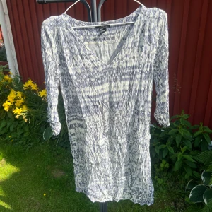 Mönstrad klänning från H&M - Klänning från H&M i vitt och blått mönster. Kortare modell med  v-ringning och trekvartsärm. 