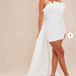 FashionNova vit klänning - Superfin vit axelbandslös klänning med kort framsida och långt släp bak. Dekorerad med 3D-blommor upptill och snörning i ryggen för perfekt passform. Släpet går att ta bort, prislappen finns kvar på kunde ej returneras. Köpt för 1450kr. Storleken går att justera, storleken är M men passar perfekt för mig som är 36