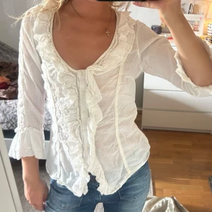 Vit volangskjorta med spetsdetaljer - Supersöt vit skjorta med volanger. Använd få gånger så i väldigt bra skick! 