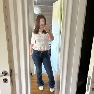 Blå bootcut jeans med låg midja - Snygga blå jeans med bootcut och låg midja. Jeansen har klassisk femficksdesign, dragkedja och knapp framtill. Materialet är jeans med en mörkblå tvätt och lätt slitning. Perfekta för en trendig och avslappnad look. Finns lite slitningar längst ner skriv för bild. Storlek 170 men passar mig som är en S.