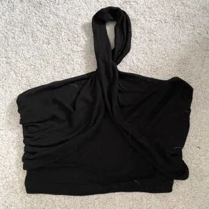 Svart halterneck tubtopp från NA-KD - Snygg svart tubtopp med halterneck och twistad detalj framtill från NA-KD. Toppen är ärmlös och har en croppad passform som sitter tight. Perfekt för dig som gillar minimalistisk stil och vill ha något enkelt men ändå trendigt.
