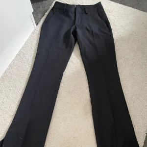 Svarta kostymbyxor med slits från BikBok - Snygga svarta kostymbyxor med slits från BikBok. Perfekta till en dressad look och funkar lika bra till skjorta som till en enkel t-shirt. Byxorna har sidfickor och är i ett mjukt, välsittande material.