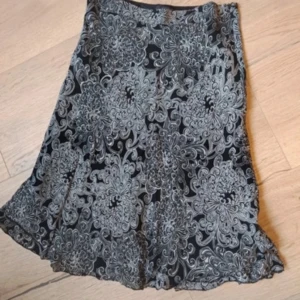 Svart kjol med blommigt mönster - Supersnygg svart kjol med stora, detaljerade blommor i vitt. Kjolen har lätt utsvängd form och vågig nederkant. Carrie bradshaw stil.