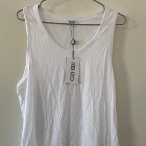 *NY*Vitt linne från Kenzo i stl XL, Presenttips  - Linne från Kenzo, modell Classic Tshirt. Ej genomskinligt. Material: Modal 67% Bomull 33% Nypris: 399 SEK, Pris nu: 85 SEK  Modellen är något kortare fram o längre bak. Luftigt, rymlig modell,  tunt, mjukt material, kenzologga längst ned.