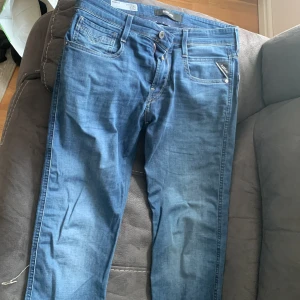 Blå Replay Anbass jeans slim fit - Säljer ett par blå Replay Anbass jeans i slim fit med klassisk femficksdesign och snygga detaljer på bakfickorna. Byxorna har dragkedjegylf och läderpatch med Replay-logga bak i midjan.