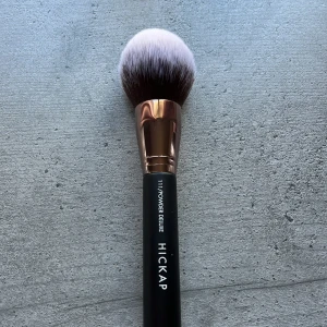 Hickap Powder Deluxe 111 sminkborste - Stor och fluffig puderborste från Hickap med svart handtag och roséguldsfärgad metall. Borsten är tät och mjuk, perfekt för applicering av puderprodukter i ansiktet. Modellnamn: 111/Powder Deluxe. Har aldrig använts.