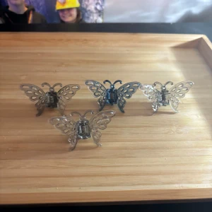 Fjärilsformade hårklämmor i plast - Fyra små hårklämmor i form av fjärilar, tillverkade i transparent och blå plast. Perfekta som accessoar för att sätta upp håret på ett lekfullt sätt.