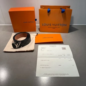 Svart LV bälte - Säljer ett Louis Vuitton bälte i svart med diskret rutig design och silverfärgat LV-spänne. Bältet har insida i ljust skinn och klassisk Louis Vuitton-logga. Kommer med originalpåse, box och kvitto.