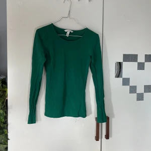 Grön långärmad topp från H&M - Säljer en enkel och stilren grön långärmad topp från H&M. Modellen är figurnära med rund halsringning och passar perfekt till lager-på-lager eller som den är. Tunn och mjuk bomullskvalitet.
