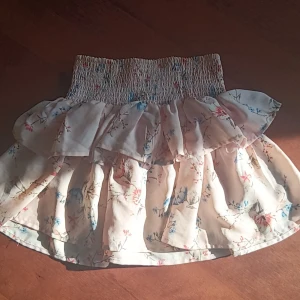 Rosa blommig kjol med volang - Charmig rosa kjol med blommigt mönster och volangdetaljer. Perfekt för en somrig look med sin korta längd och elastiska midja för bekväm passform.