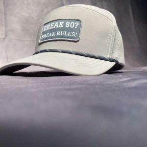 Ljusgrå keps med text 'BREAK 80? BREAK RULES!' - Snygg ljusgrå keps med böjd skärm och patch framtill med texten 'BREAK 80? BREAK RULES!'. Kepsen har perforerade sidor för extra ventilation och en dekorativ rand längs skärmens kant.