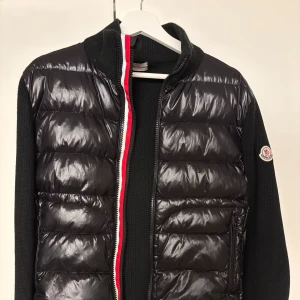Moncler cardigan - Säljer en svart cardigan från Moncler med stickade ärmar och quiltad front som tyvärr inte används längre. Jackan har två olika dragkedjor som ni kan se på bilderna. Pris kan diskuteras vid snabb affär och tveka inte att höra av er! 