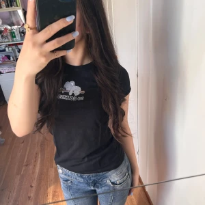 Svart t-shirt med tryck från F.A. Sister - Svart t-shirt från F.A. Sister med ett litet vitt tryck framtill som föreställer en molnig himmel och texten 'do nothing'. T-shirten har rund halsringning och korta ärmar. Perfekt till jeans eller shorts.