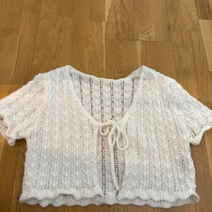Vit stickad bolerotopp med knyt - Superfin vit stickad bolerotopp med korta ärmar och knyt framtill. Toppen har ett luftigt stickat mönster och volangkant nedtill, perfekt för lager-på-lager-stil.