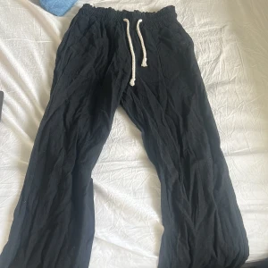 Svarta linnebyxor med dragsko - Svarta, lösa linnebyxor med vit dragsko i midjan. Byxorna har raka ben och fickor både fram och bak. Perfekta för en avslappnad stil och sköna att bära varma dagar.