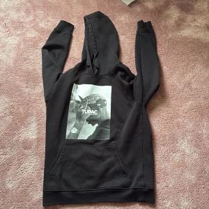 Svart Tupac hoodie från Mister Tee - Säljer en svart hoodie från Mister Tee med stort Tupac-tryck på bröstet. Det står storlek L men den passar parfekt M