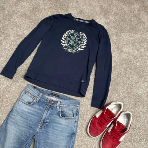 Tröja - Mörkblå sweatshirt med rund hals och tryckt emblem i grönt och vitt på bröstet.  Storlek M men passar även S. Köp för endast 199.