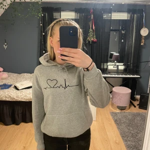 Grå hoodie med hjärtslag-tryck - Säljer en ljusgrå hoodie med hjärtrytm på framsidan samt en ficka på magen. Använd några gånger men fortfarande som ny!