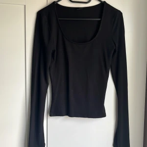 Svart långärmad topp från Gina Tricot - En svart långärmad topp från Gina Tricot med rund, djup urringning och slits vid ärmslut. Enkel och stilren design i mjukt bomullsmaterial, perfekt att matcha med olika outfits.