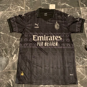 AC Milan svart bortatröja Puma - Snygg svart AC Milan bortatröja från Puma med silvriga detaljer och loggor. Kortärmad modell med klubbmärke och sponsortryck på bröstet samt mönstrad front. Perfekt för fotbollsfans som vill sticka ut på läktaren.