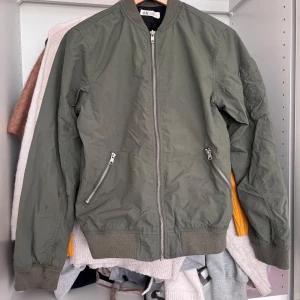 Olivgrön bomberjacka från H&M - Säljer en olivgrön bomberjacka från H&M med dragkedja framtill och två snedställda fickor med dragkedja. Jackan har ribbade muddar vid ärmslut, krage och nederkant. Klassisk och stilren modell som passar till mycket. Lite smutsig kan skicka mer detaljerade bilder på vart om ni är intresserade💕