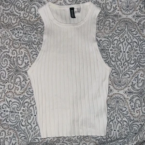 Vit ribbad linne - Säljer en vit ribbad linnetopp från HM. Toppen har en hög halsringning och är ärmlös med en tight passform. Helt ny aldrig använd.