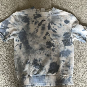 Nike batikmönstrad sweatshirt - Säljer en kortärmad sweatshirt från Nike med batikmönster i blått och vitt. Tröjan har rund halsringning och ribbade muddar vid ärmslut och nederkant. Liten Nike-logga broderad på bröstet.
