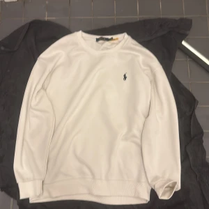 Vit sweatshirt från Polo Ralph Lauren det är xl men känns som L - Säljer en klassisk vit sweatshirt från Polo Ralph Lauren med den ikoniska broderade loggan på bröstet. Tröjan har rund halsringning, långa ärmar och ribbade muddar vid ärmslut och nederkant. Perfekt för en stilren och enkel look.