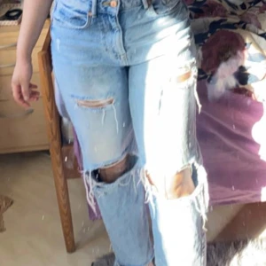 Ljusblå ripped jeans - Säljer ett par ljusblå jeans med flera stora slitningar och hål på benen. Jeansen har hög midja och raka ben med råa kanter nertill. Perfekta för sommaren.