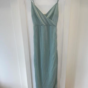 Ljusblå glittrig långklänning från Trendyol - Supersnygg ljusblå långklänning med smala axelband och v-ringning från Trendyol. Har även en slits. Klänningen har ett glittrigt tyg som ger en festlig känsla och en elegant omlott-detalj framtill. Perfekt för speciella tillfällen! Bara använd 1 gång. 