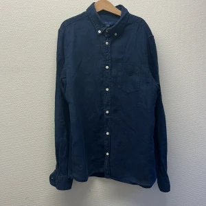 Gant linneskjorta  - Säljer en stilren mörkblå skjorta från Gant i linne. Skjortan har klassisk krage, vita knappar och en bröstficka med broderad Gant-logga. Den är i bra skick och är sällan använd. Skjortan har inga defekter. Den är i storlek 158-164 men passar xs. Tar ej imot byten. Det är först till kvarn. Den är perfekt för sommaren.
